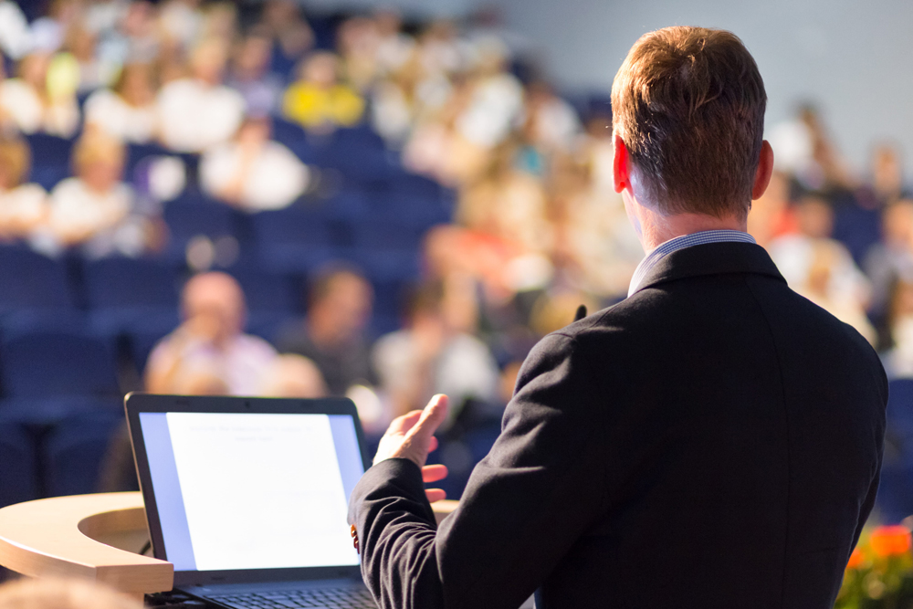 man at podium giving important sales presentation at event